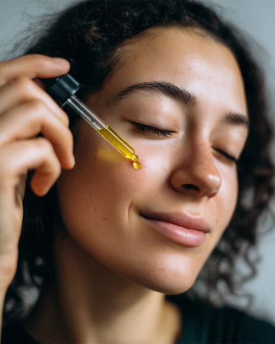 A young woman applies Sunset Face Oil with a dropper to her face