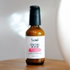 An amber glass bottle with black treatment pump of Facial Wash with Frankincense, Rose and Honey on a table.
