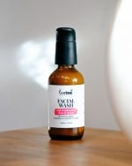An amber glass bottle with black treatment pump of Facial Wash with Frankincense, Rose and Honey on a table.