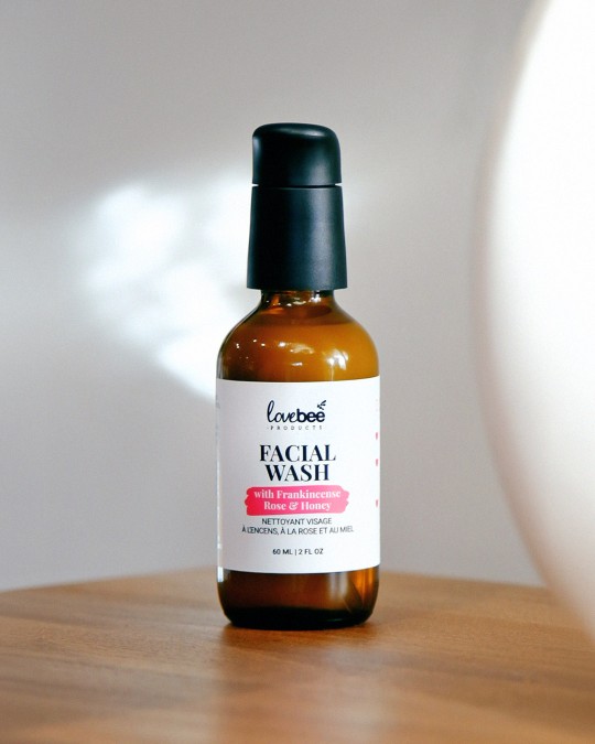 An amber glass bottle with black treatment pump of Facial Wash with Frankincense, Rose and Honey on a table.