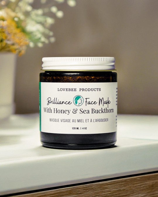 Face mask jar rests on a countertop with flowers blurred in thebackground